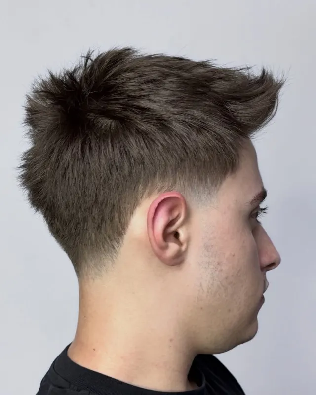 Öne dikleştirilmiş hacimli quiff, yandan görünüm; şakakta net düşük fade geçişi